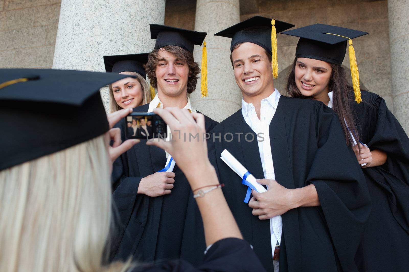 Close-up of a blonde graduate taking a picture of her friend in front of the university