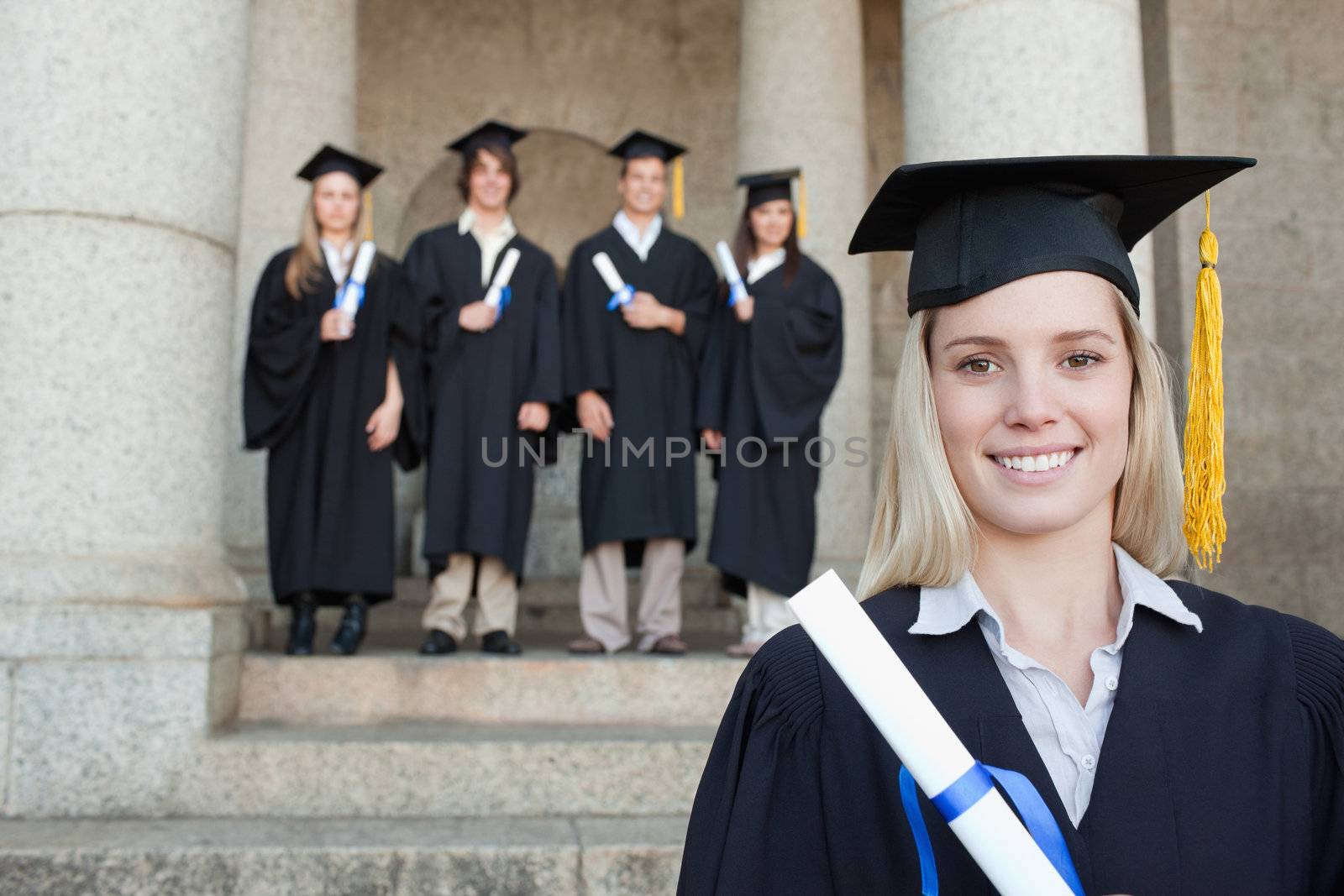 Close-up of a blonde graduate with her friends in background in front of the university