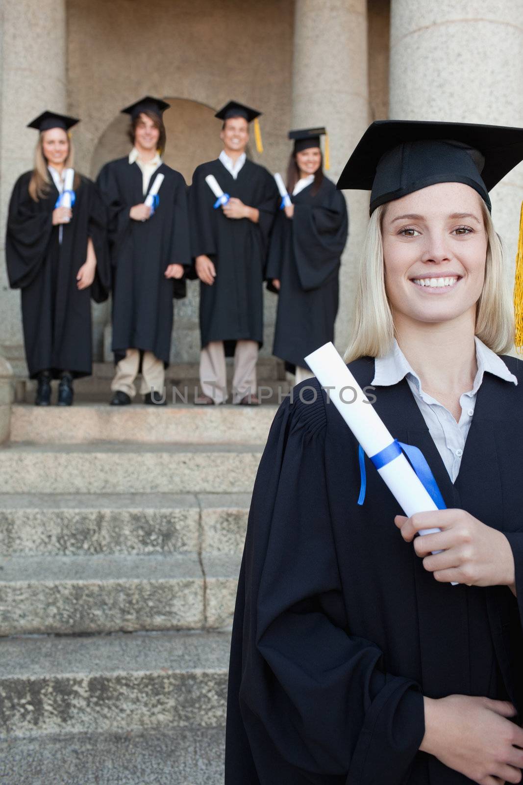Close-up of a blonde graduate smiling with her friends in background in front of the university
