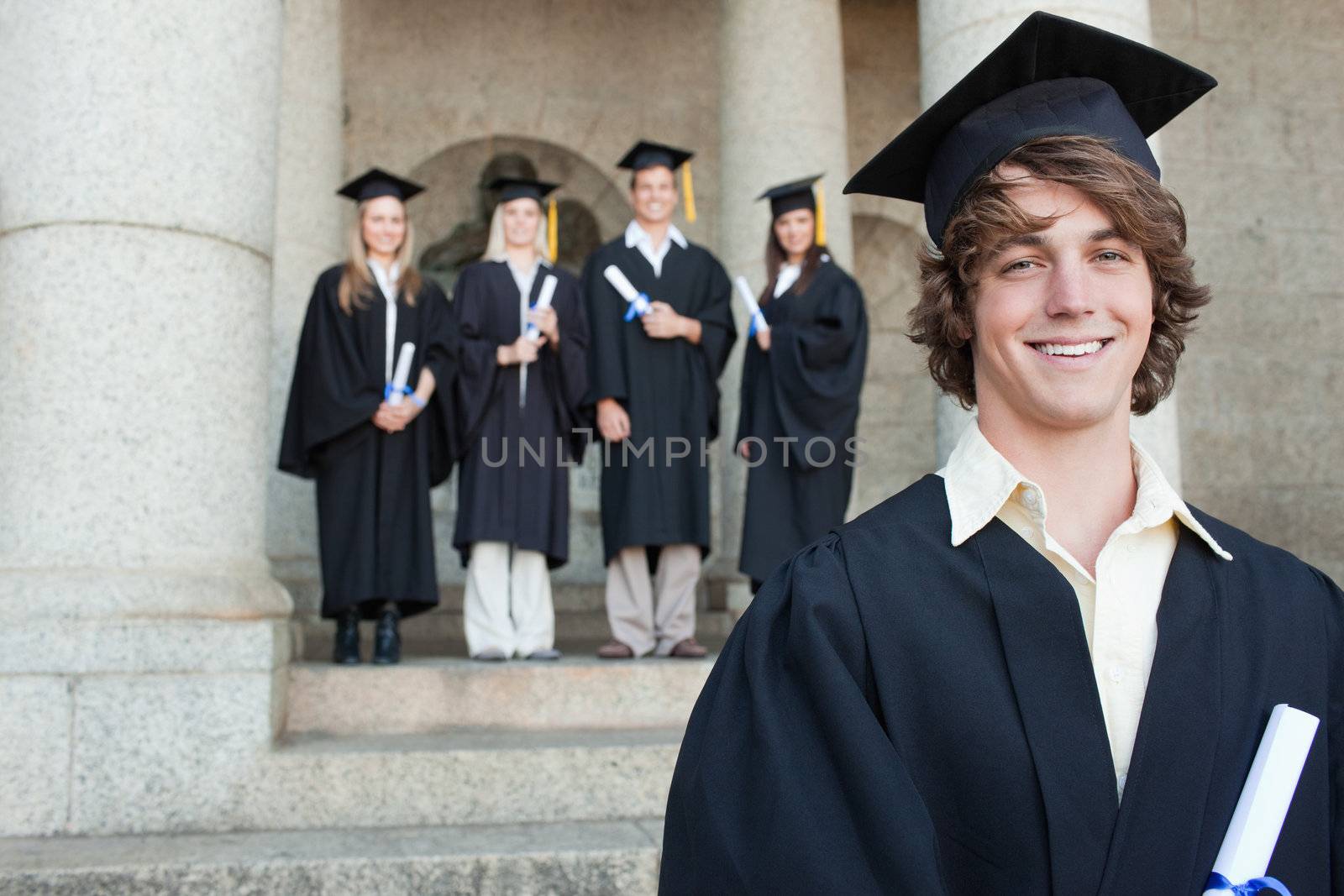 Close-up of a smiling graduate smiling with her friends in background in front of the university