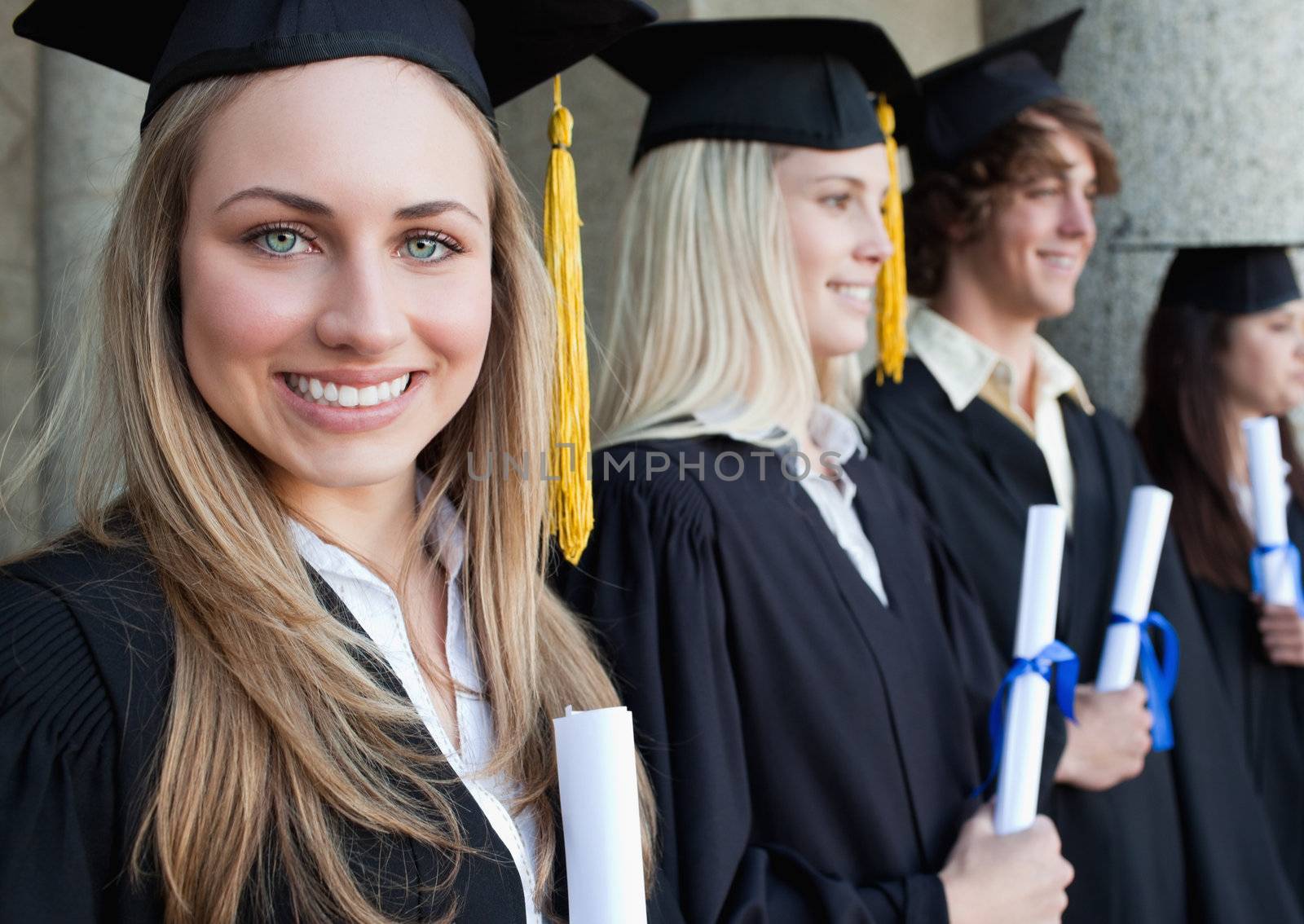 Close-up of a beautiful graduate with blue eyes next to her friends posing