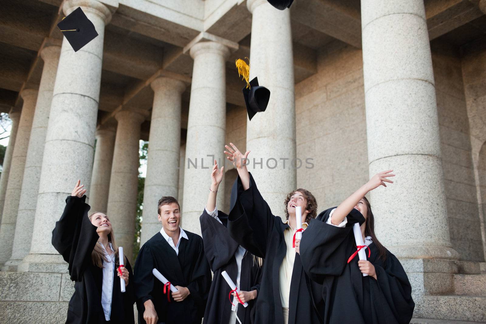 Graduates throwing their hats in the sky in front of their university