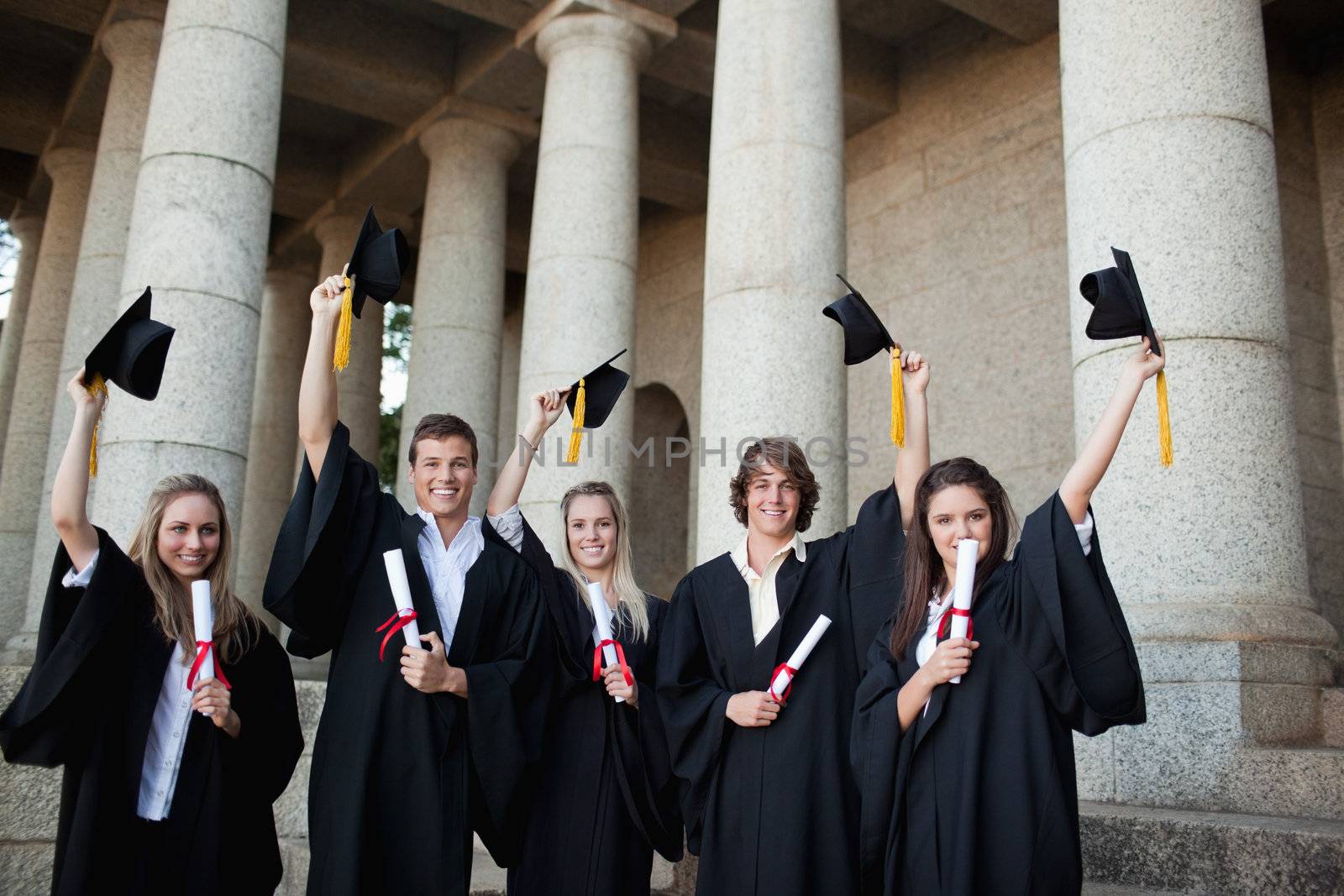 Graduates holding up their hats by Wavebreakmedia