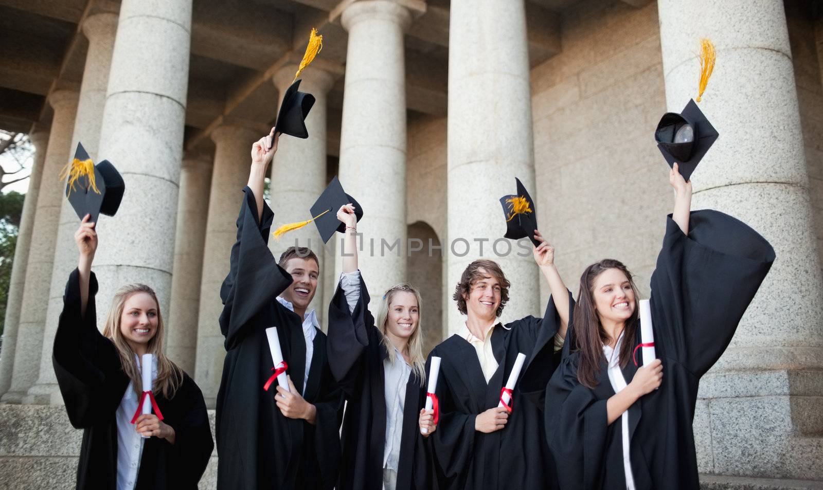 Smiling graduates holding up their hats in front of the university