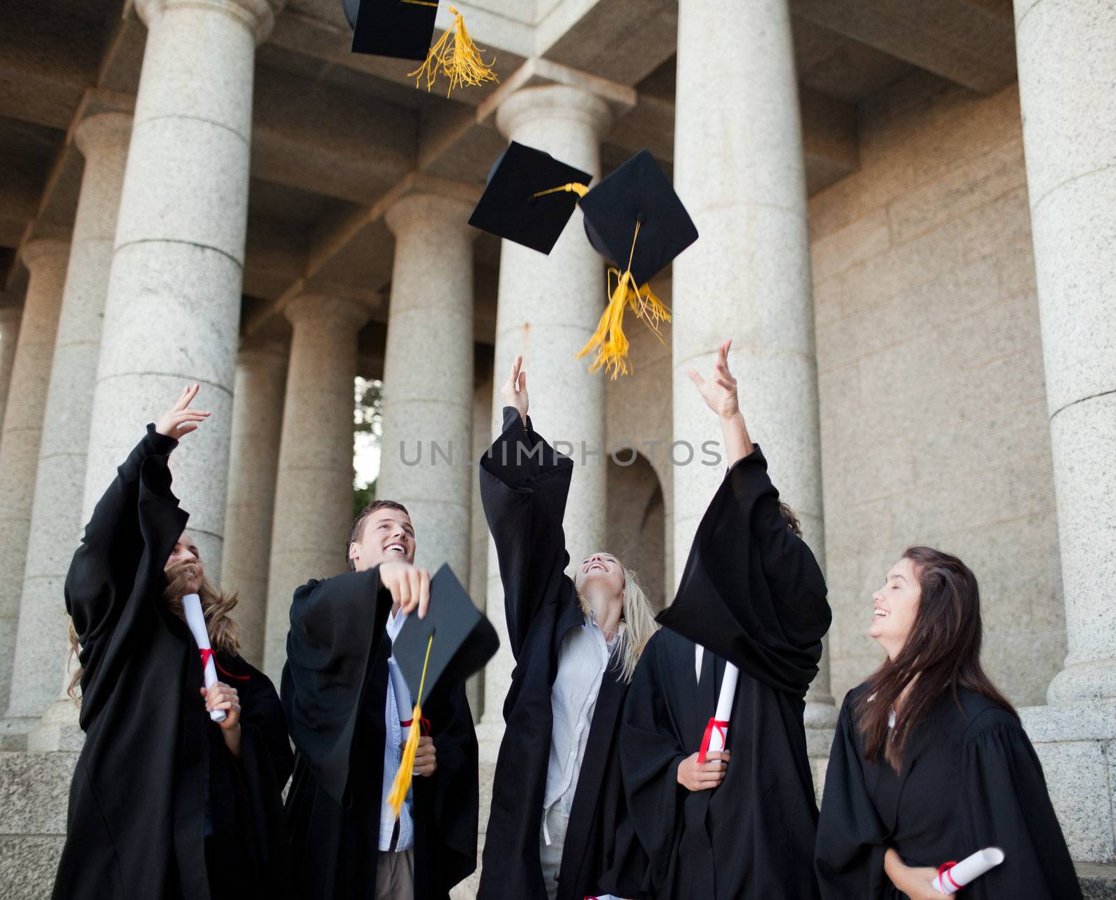 Smiling graduates throwing their hats in the sky by Wavebreakmedia