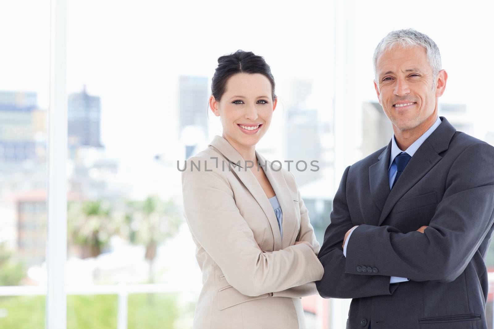 Smiling secretary and mature a director crossing their arms in front of the window