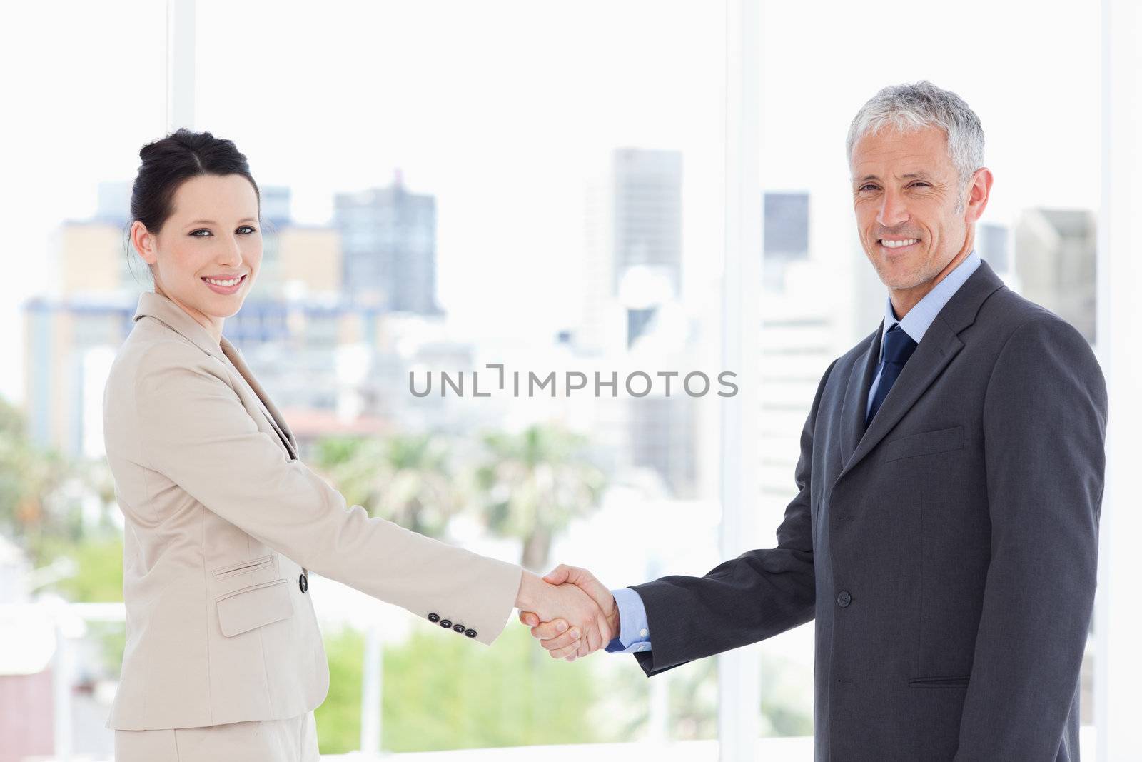 Two business people shaking hands while smiling and looking at the camera