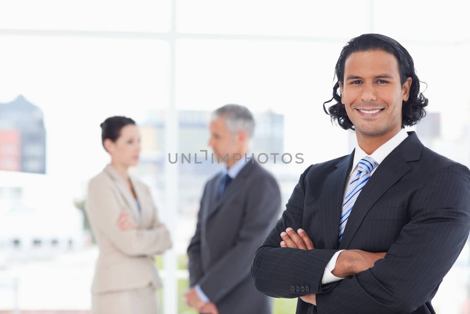 Smiling executive crossing his arms in front of two business people