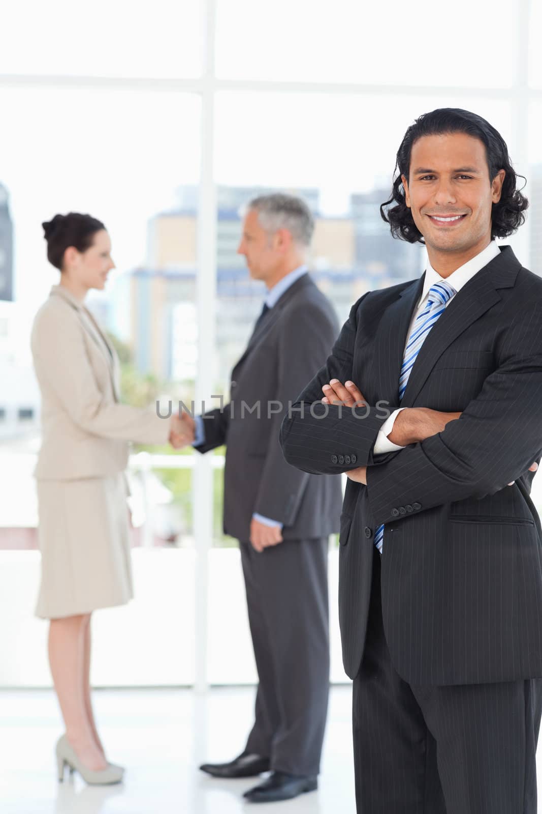Young executive standing upright in front of business people shaking hands
