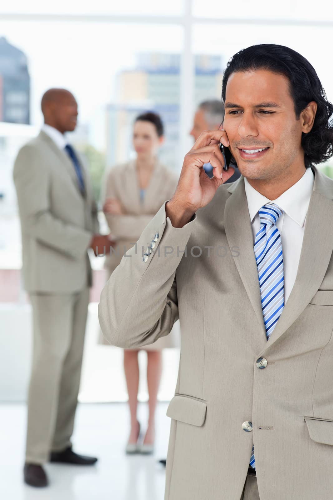 Businessman using a cell phone while his team is talking behind  by Wavebreakmedia