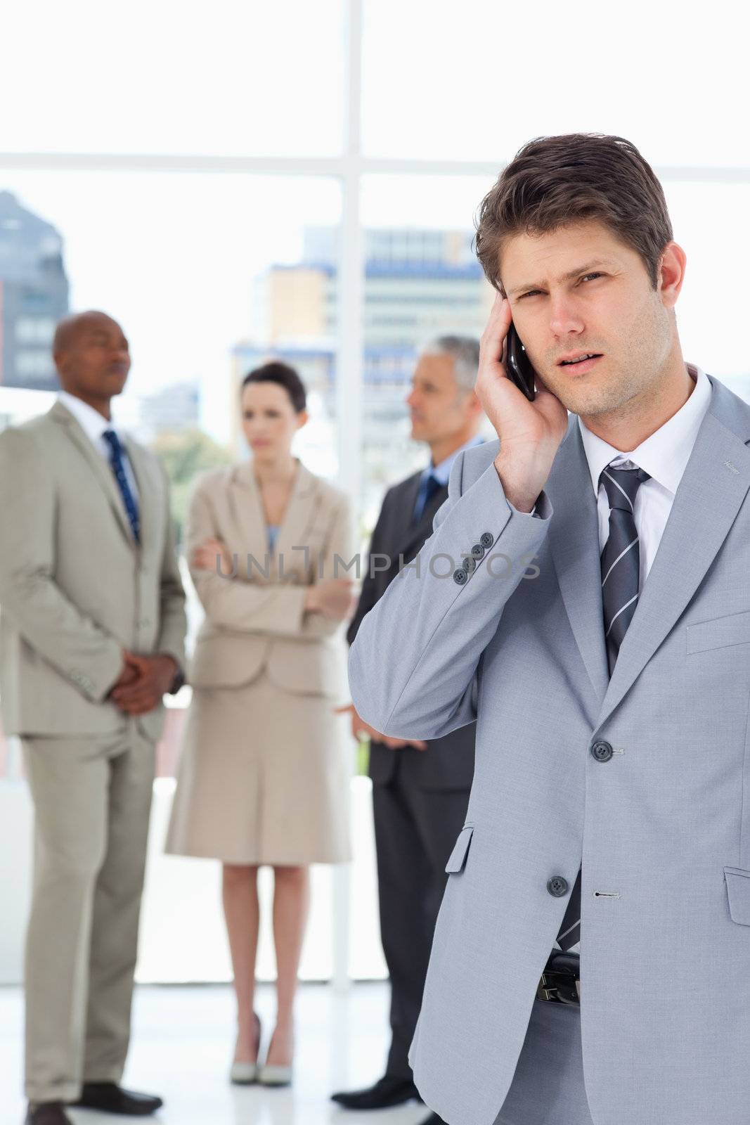 Young executive using a cell phone while his team is behind him