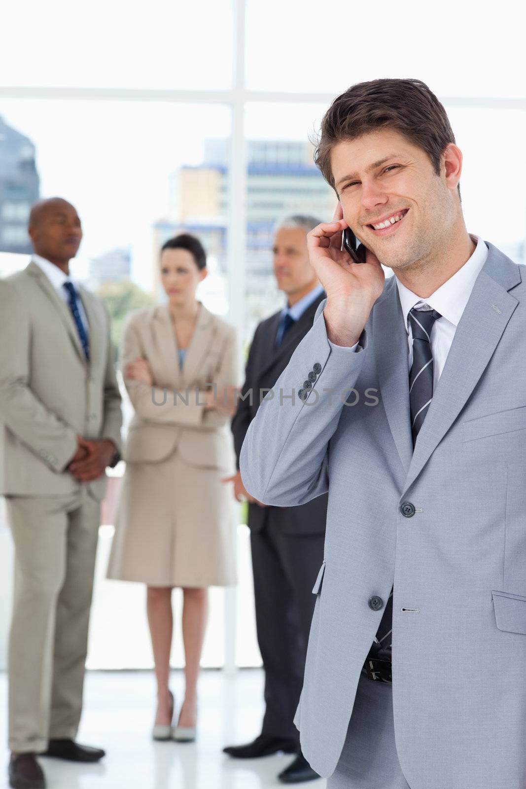 Smiling businessman using a mobile phone in front of his team by Wavebreakmedia