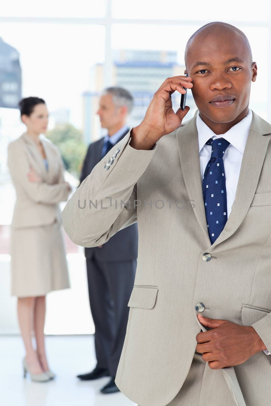 Young manager talking on the phone very seriously while his team by Wavebreakmedia