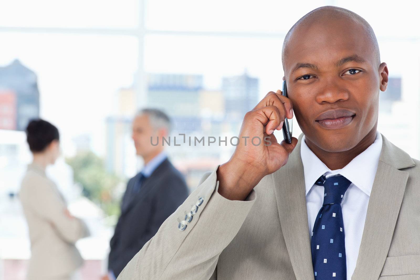 Serious businessman in a suit talking on the phone while his tea by Wavebreakmedia