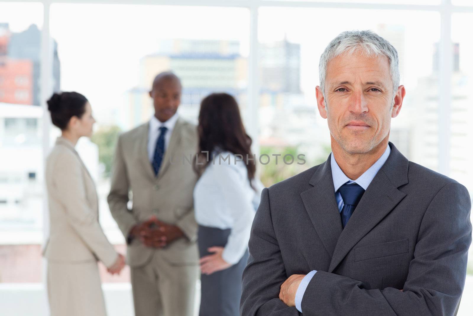 Serious manager crossing his arms while his business team is in the background