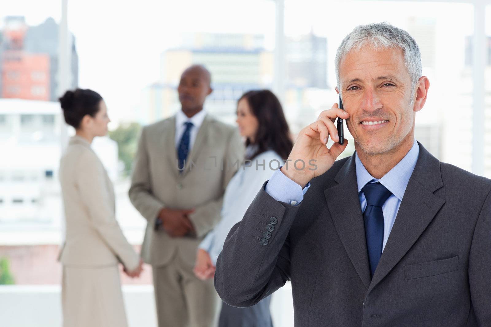 Smiling manager talking on the cell phone while his team is in the background