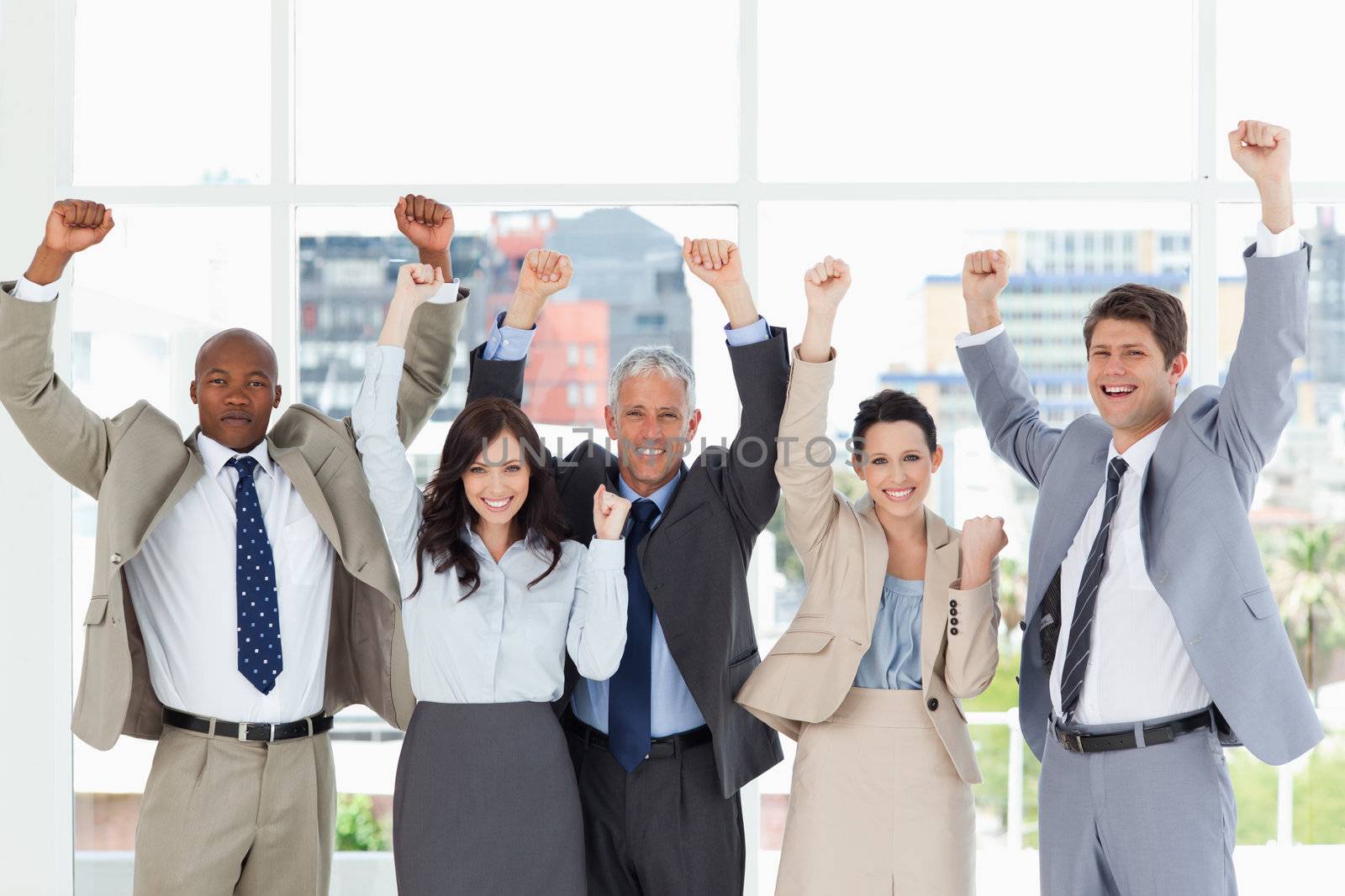 Business team smiling and standing upright with arms raised in success