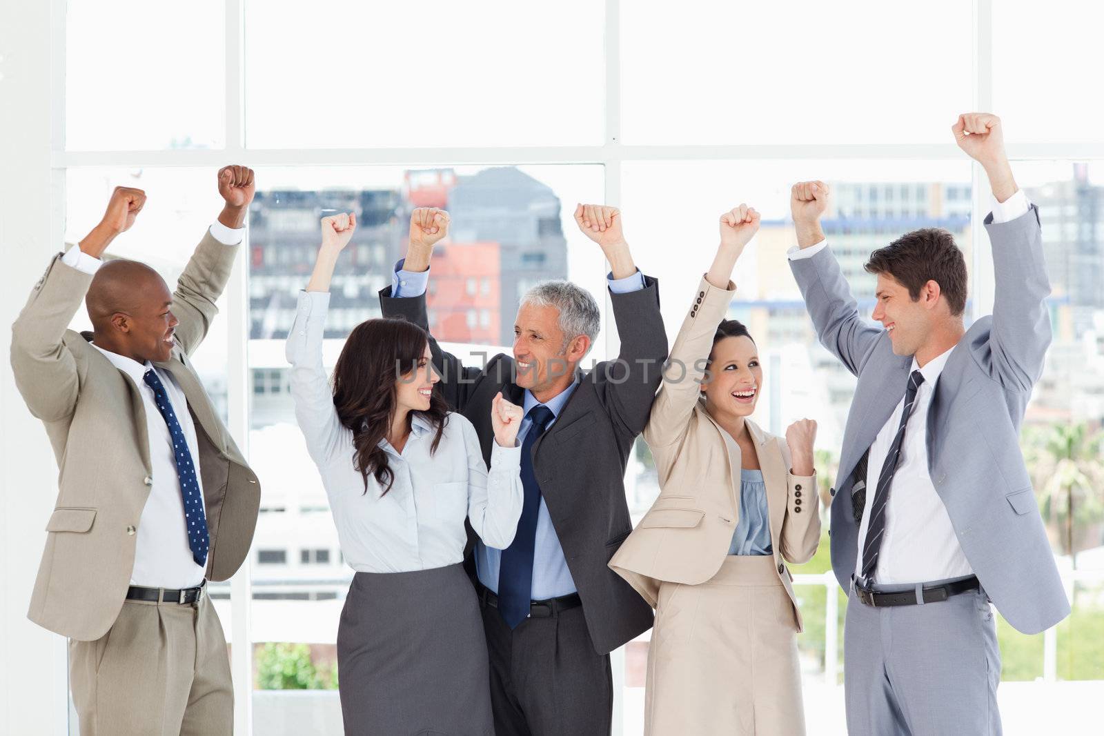 Smiling business people looking at each other and raising their arms in success