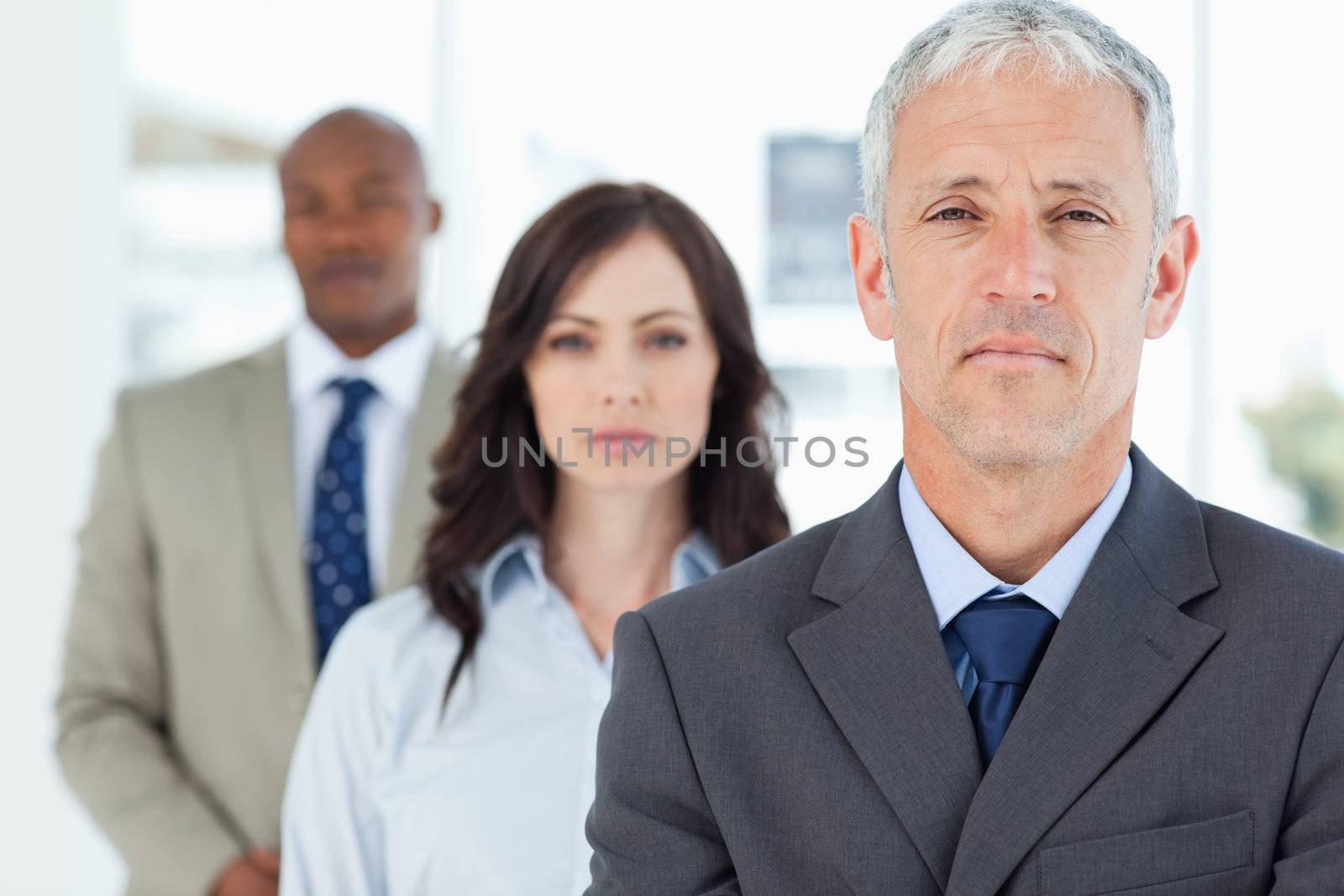 Mature manager standing upright and followed by two serious employees