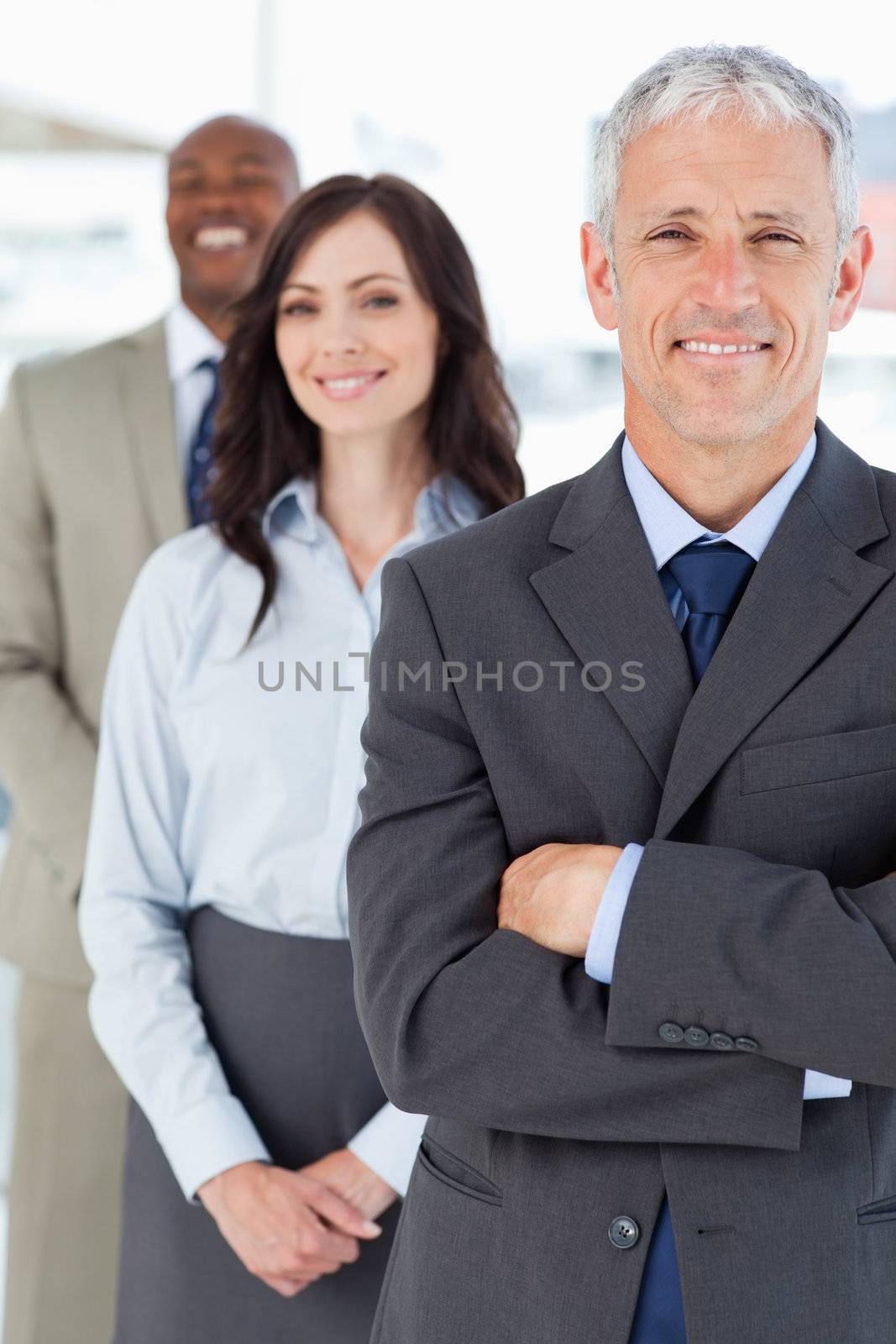 Mature smiling manager in a formal suit followed by two young business people