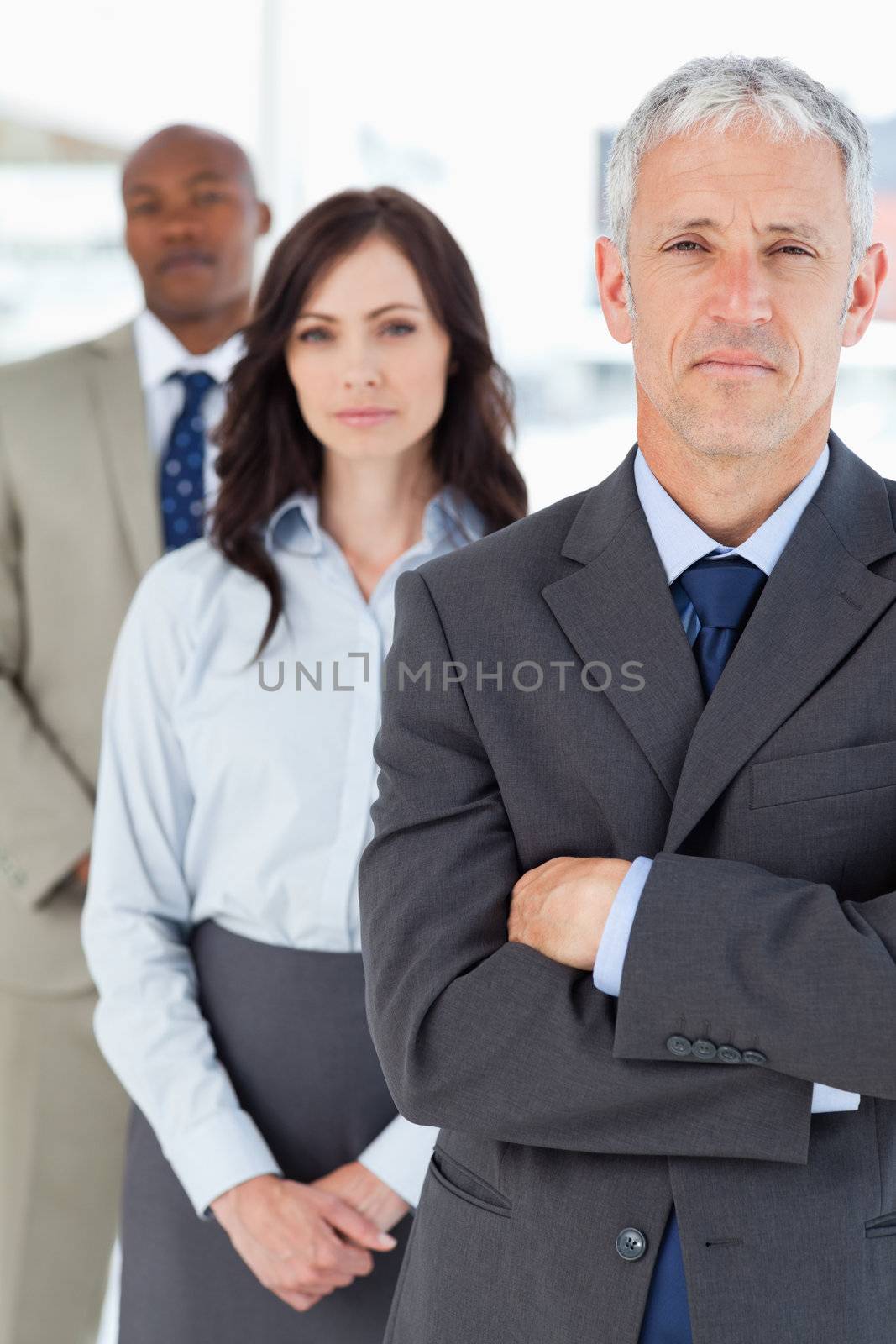 Mature manager crossing his arms seriously in front of two membe by Wavebreakmedia