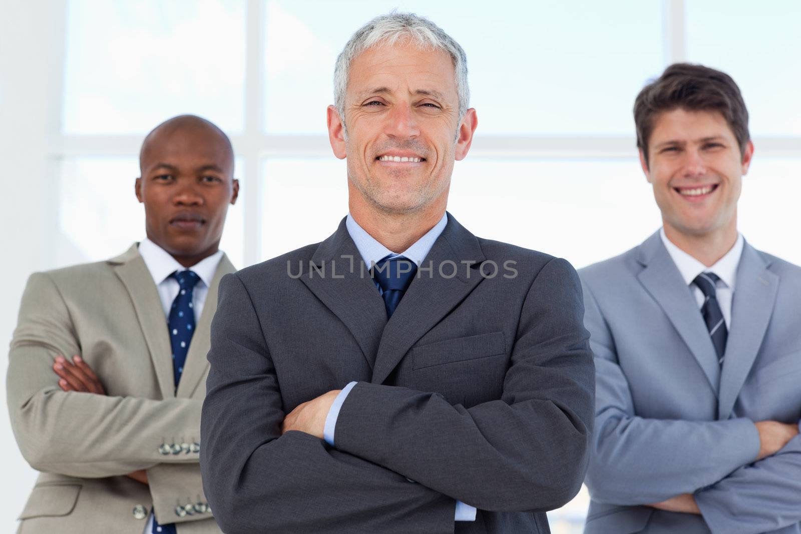 Smiling manager crossing his arms and followed by two young employees in suits