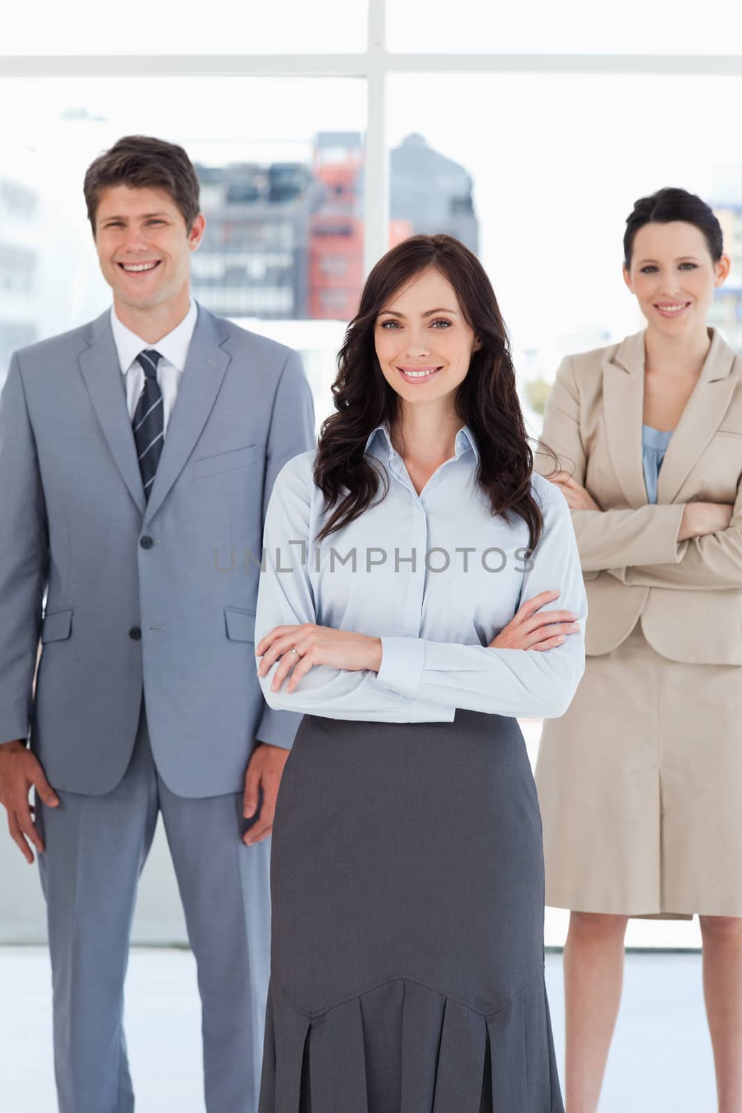 Young smiling businesswoman crossing her arms in front of two relaxed colleagues