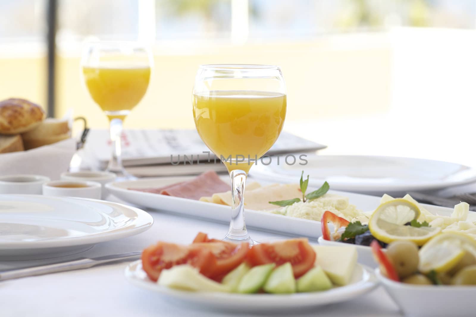Fresh orange juice on breakfast table with tomatoes, cucumber, cheeses and olives
