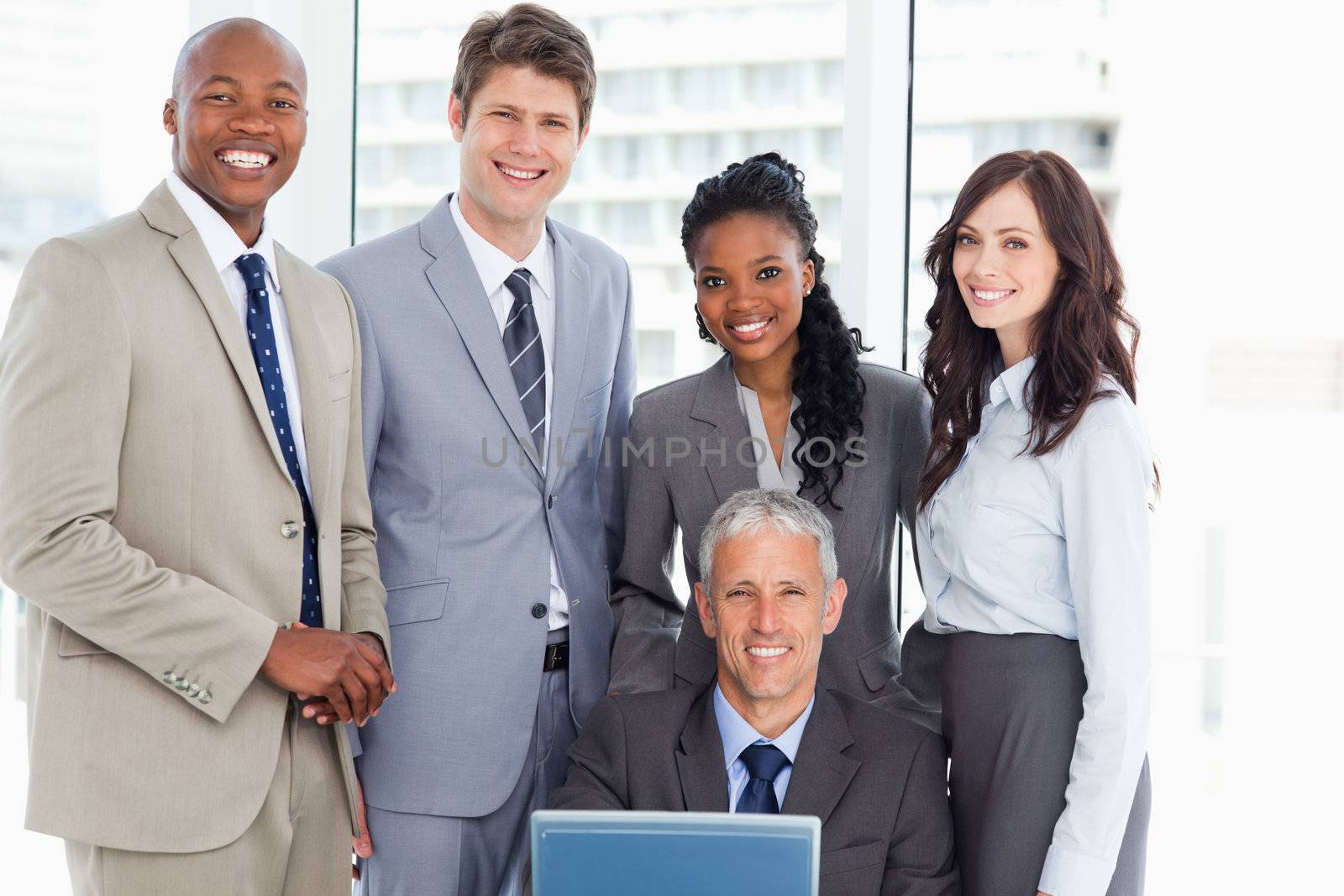 Mature manager smiling with a laptop and his business team