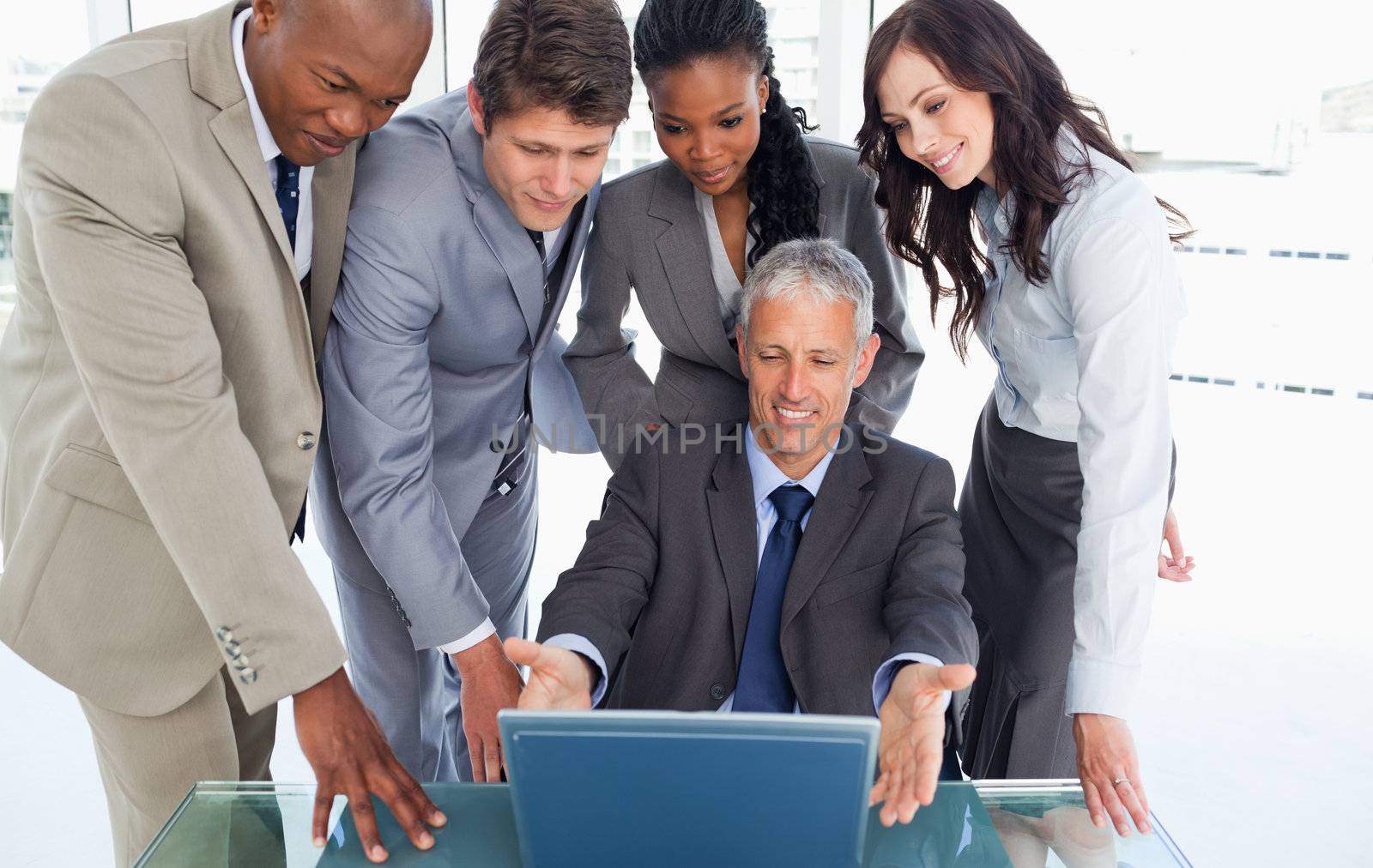 Smiling manager sitting at the desk surrounded by his earnest business team