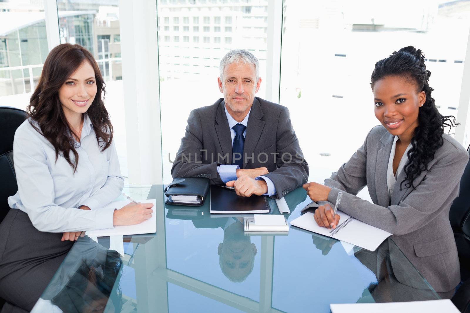 Serious director sitting at the desk and accompanied by two smiling businesswomen