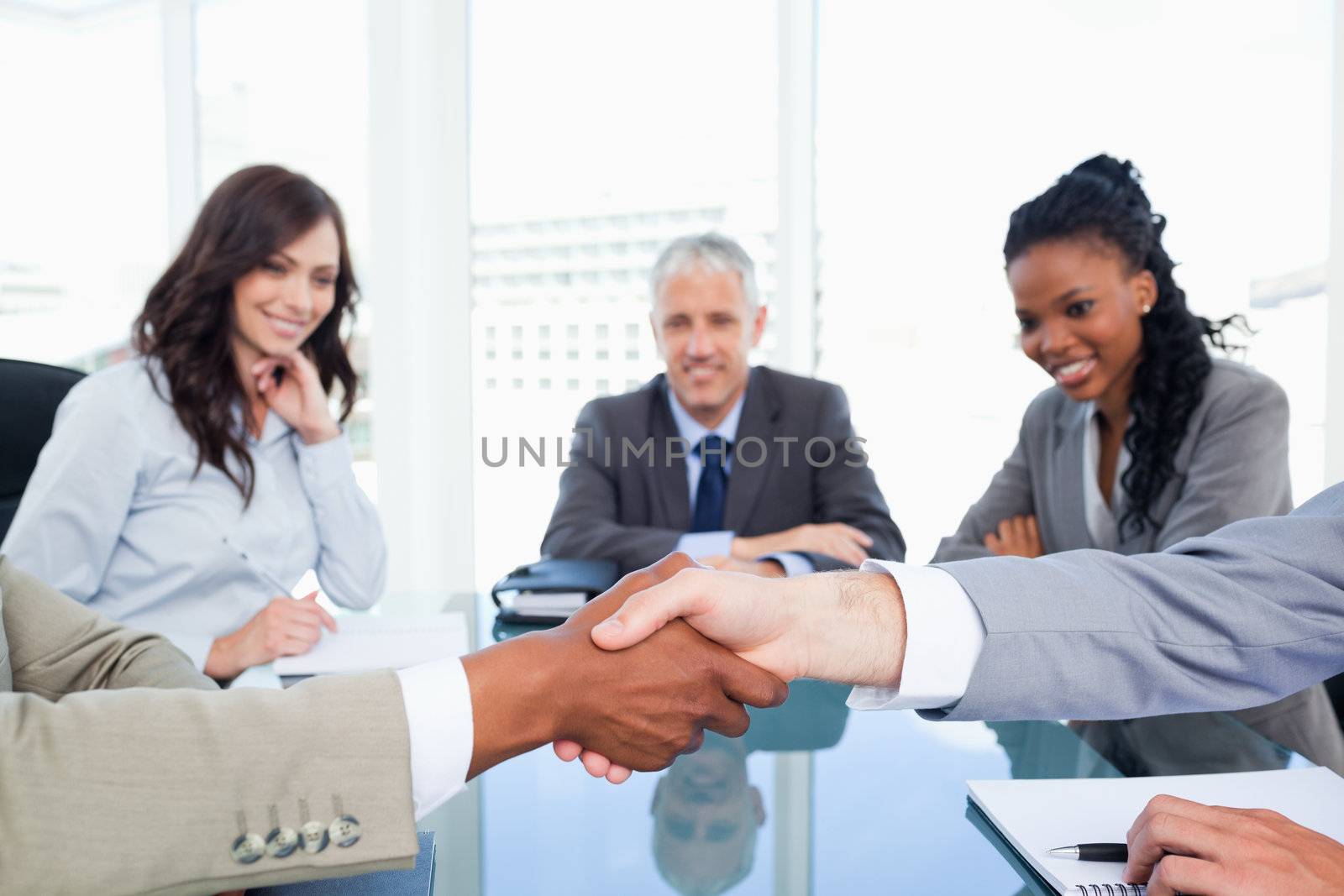 Co-workers shaking hands while their director and two executives watching them