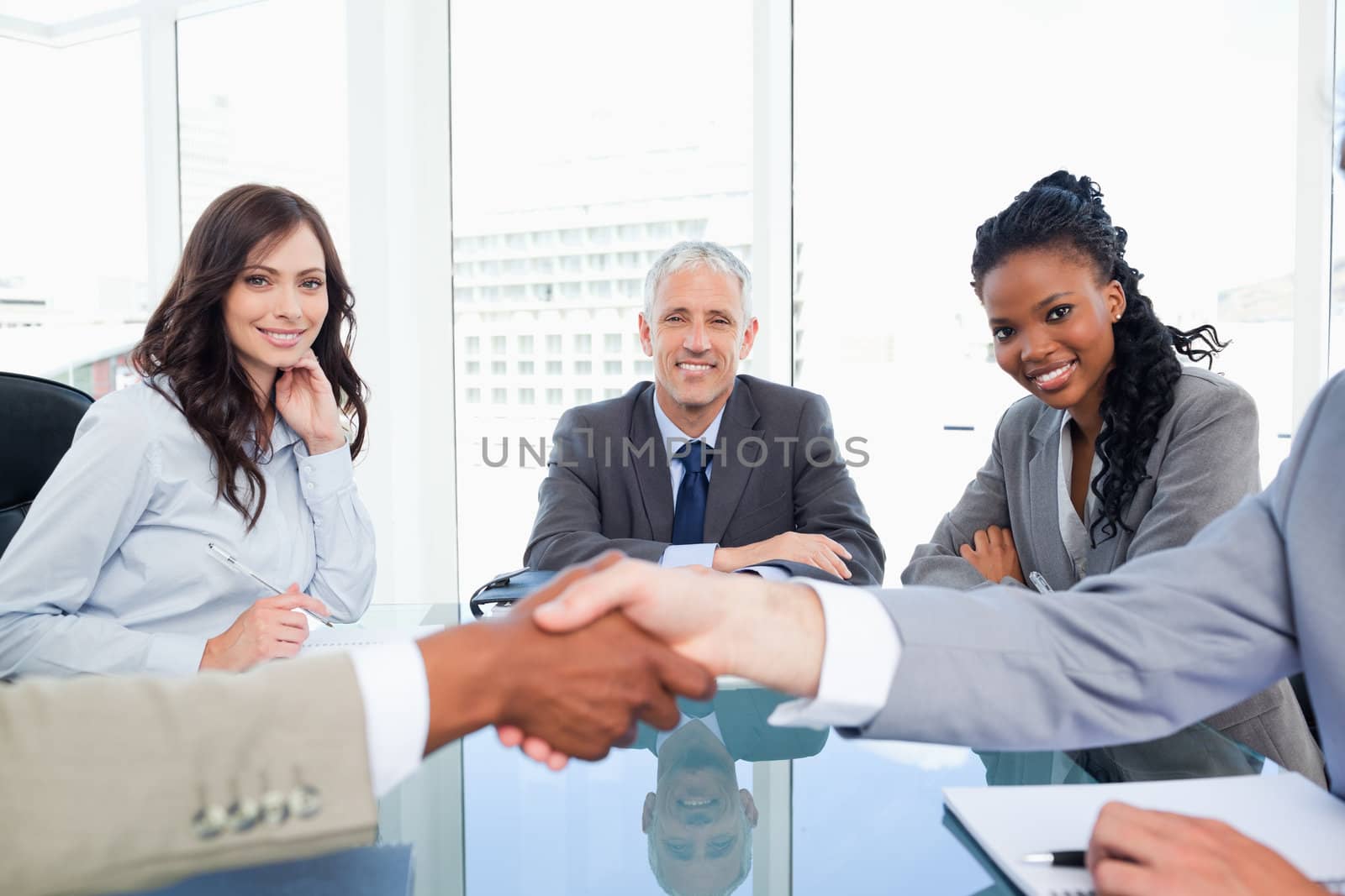 Three smiling co-workers looking at two business people shaking  by Wavebreakmedia