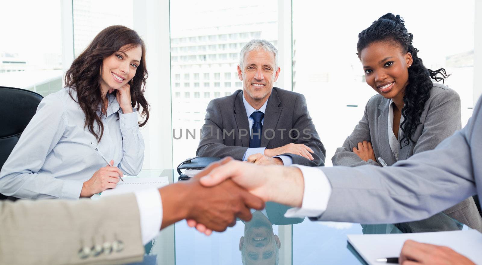 Two executives and their director smiling while looking at colleagues shaking hands