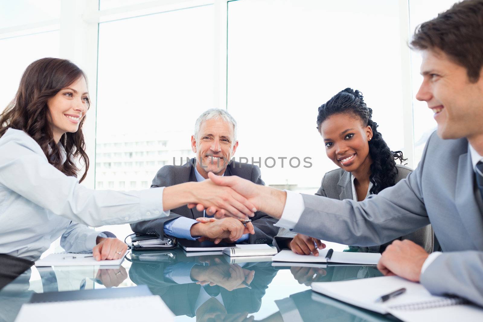 Young smiling executives shaking hands in front of their manager and a colleague