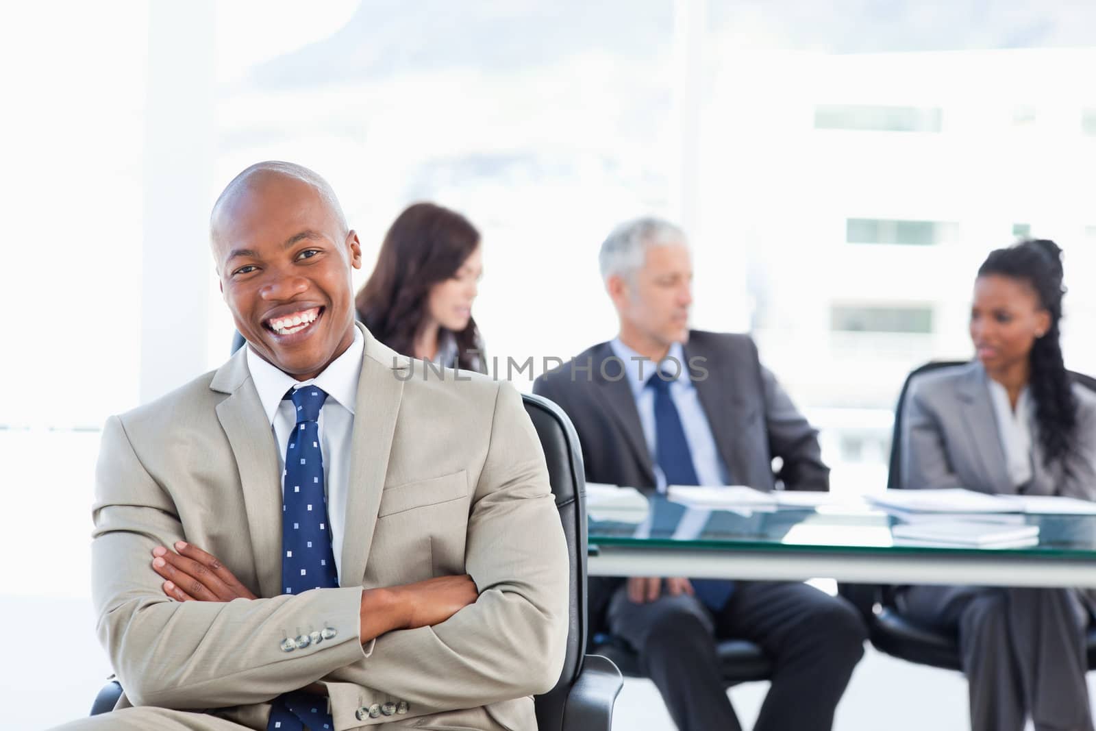 Young executive laughing while crossing his arms and sitting in front of his team