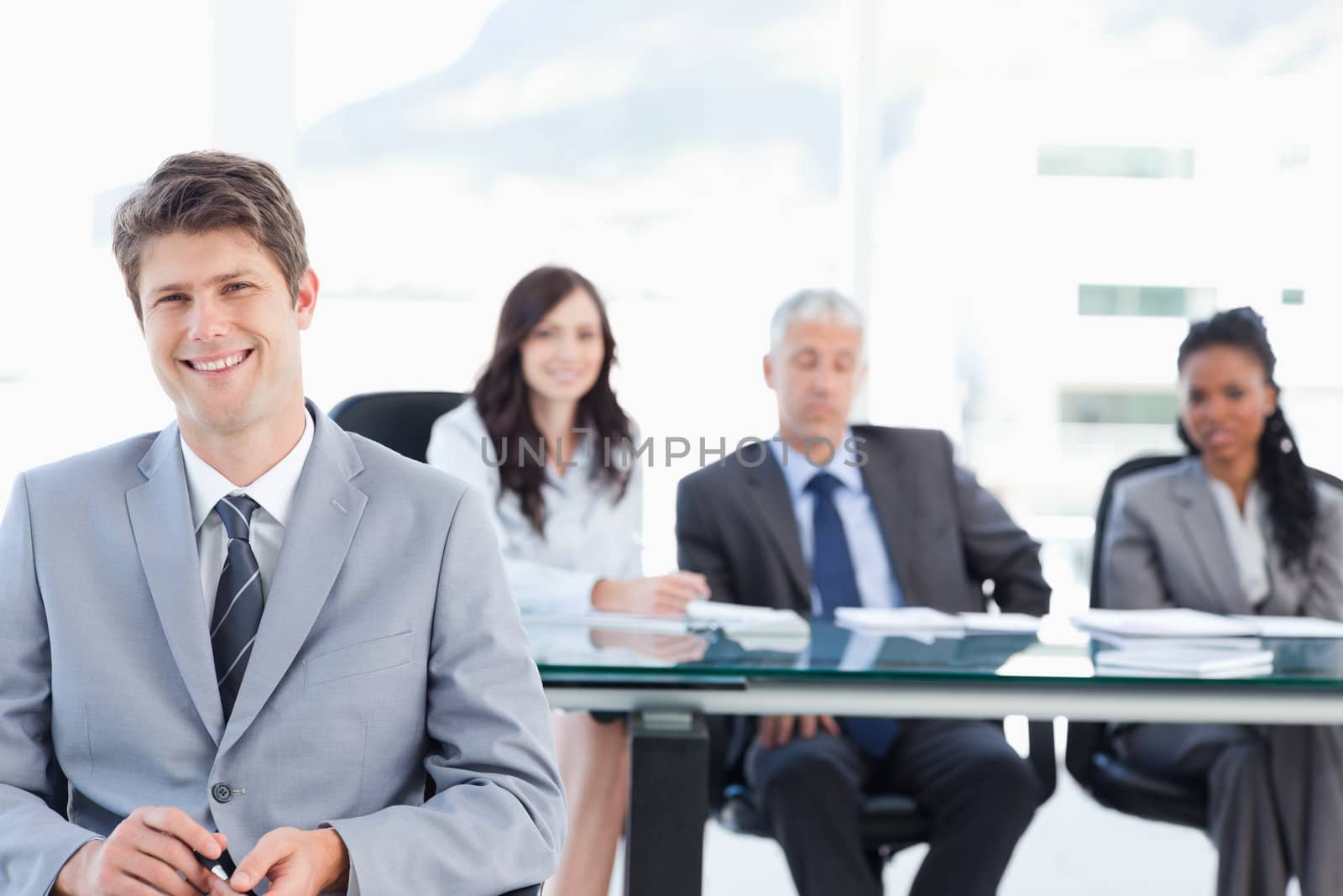 Smiling executive sitting in front of his earnest team and looking at the camera