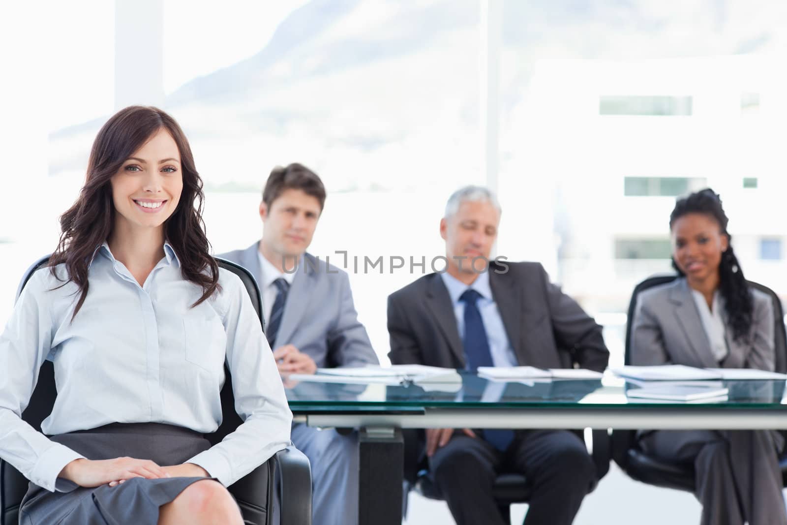 Young executive sitting with her hand on her leg and accompanied by her team in the background