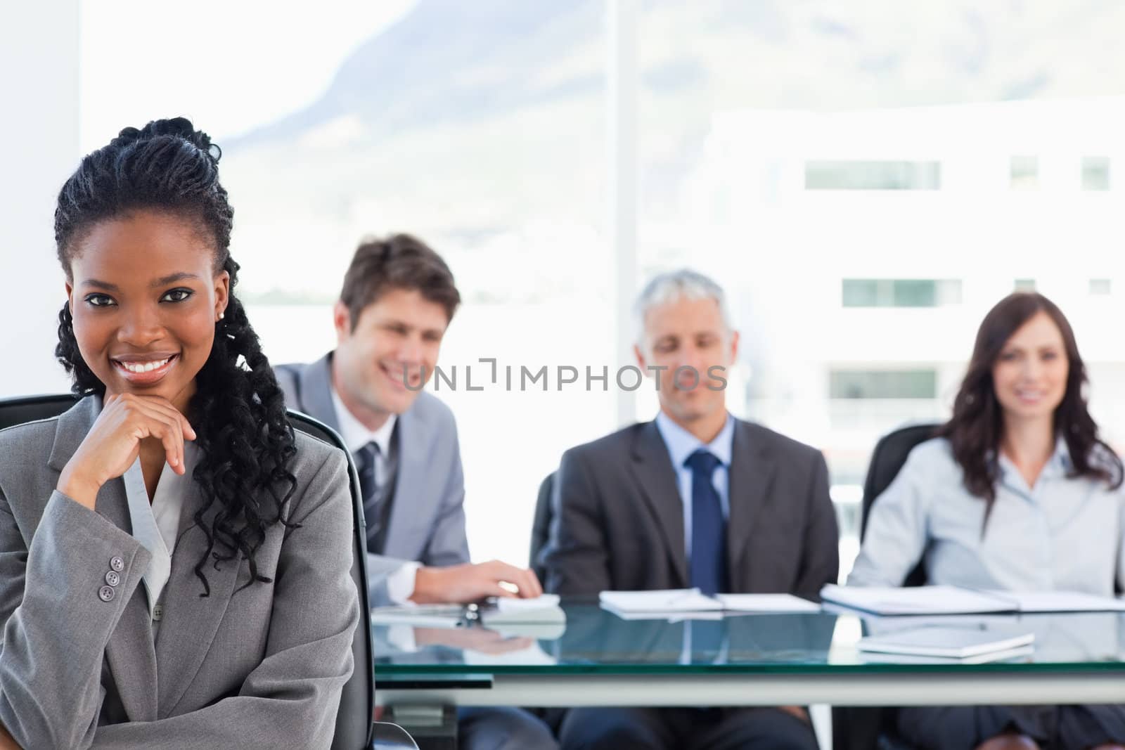 Confident smiling executive sitting in a meeting room while her team is looking at her