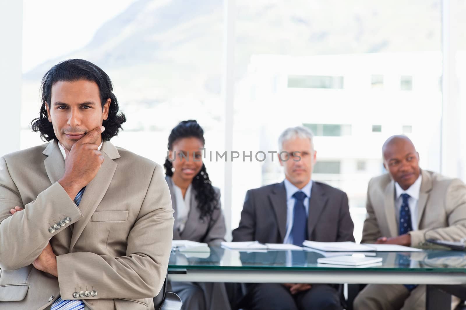 Stern businessman with his hand on his chin sitting in front of his business team