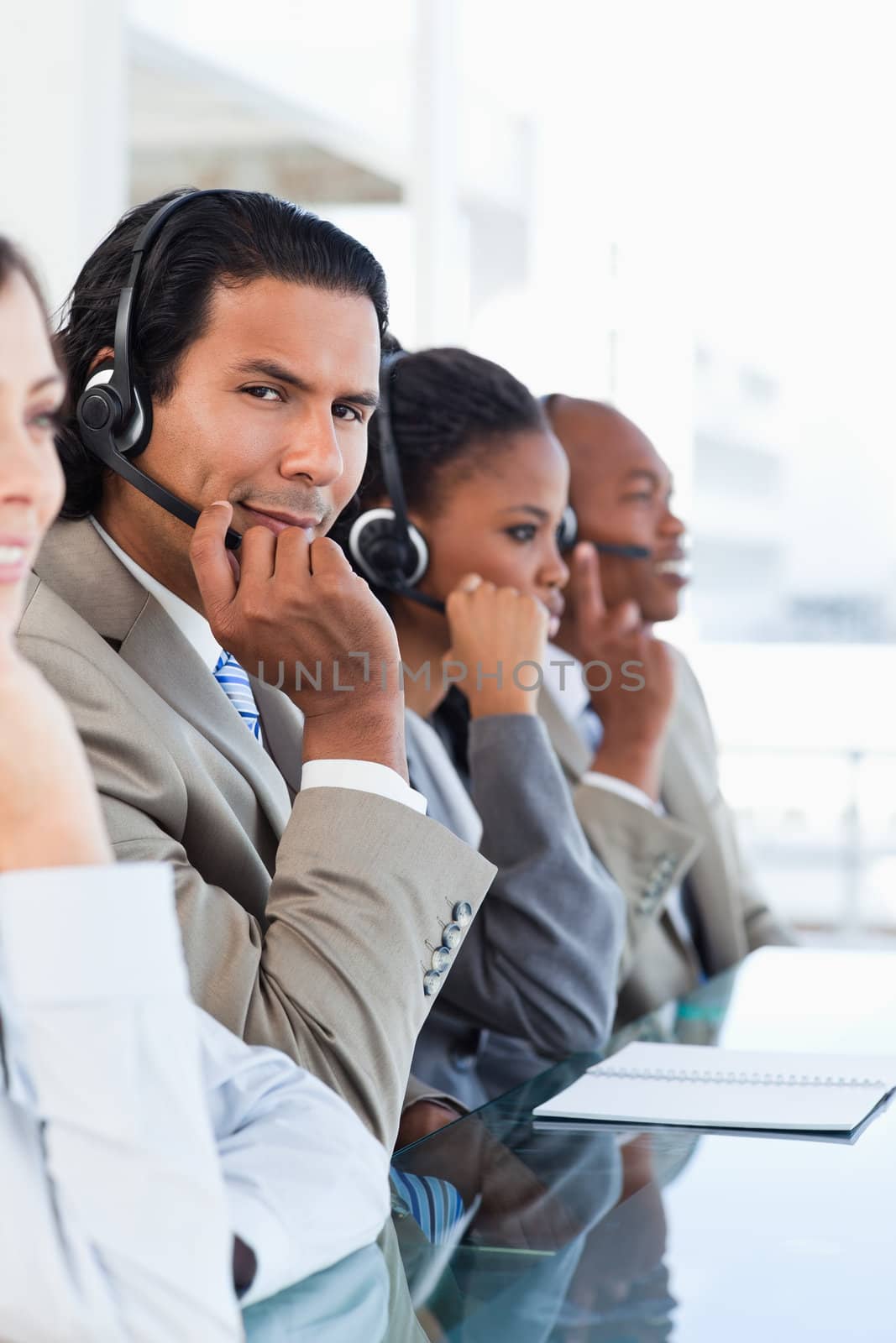 Young serious call centre employee surrounded by his working team