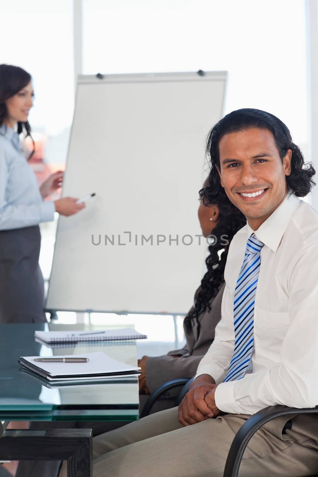 Smiling businessman sitting at a desk while listening to a prese by Wavebreakmedia