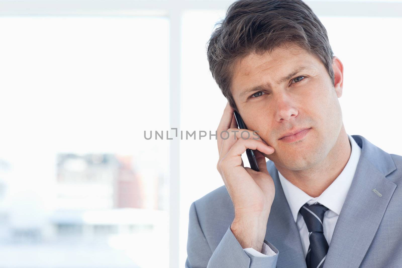 Young executive seriously calling somone in front of the window