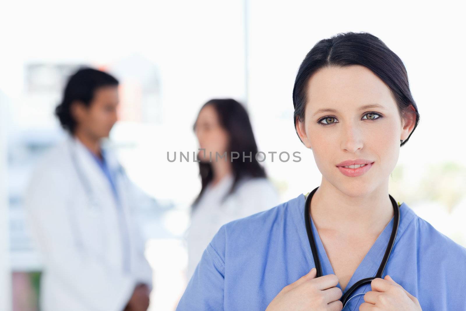 Serious intern looking at the camera while her medical team is in the background