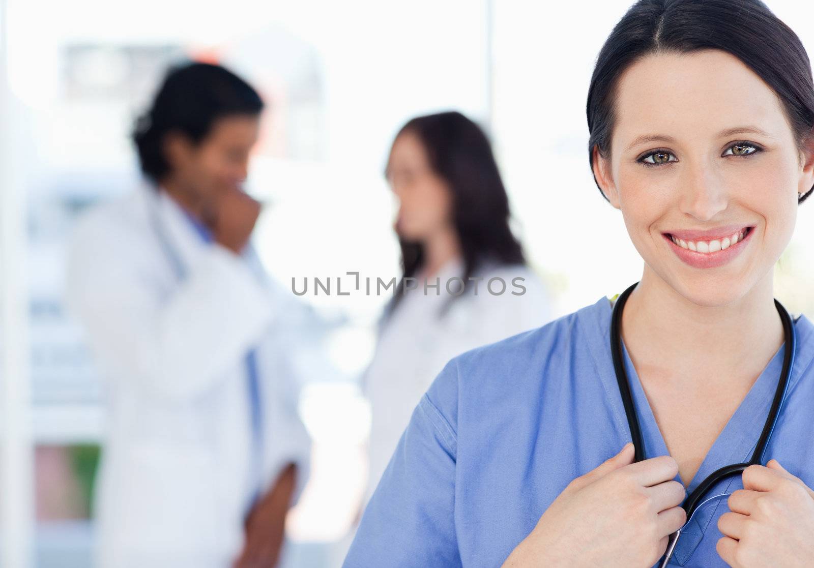 Young smiling nurse standing upright accompanied by her team who is standing behind her