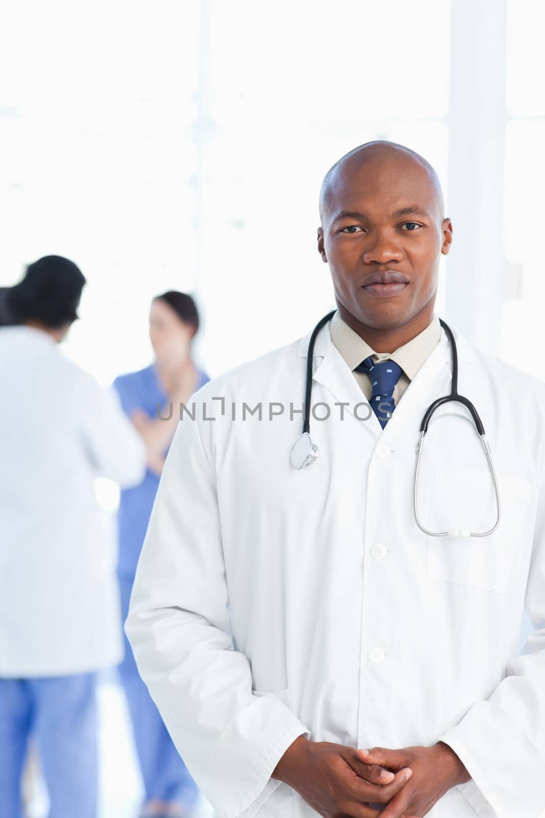 Doctor standing upright with his hands crossed and his team in t by Wavebreakmedia
