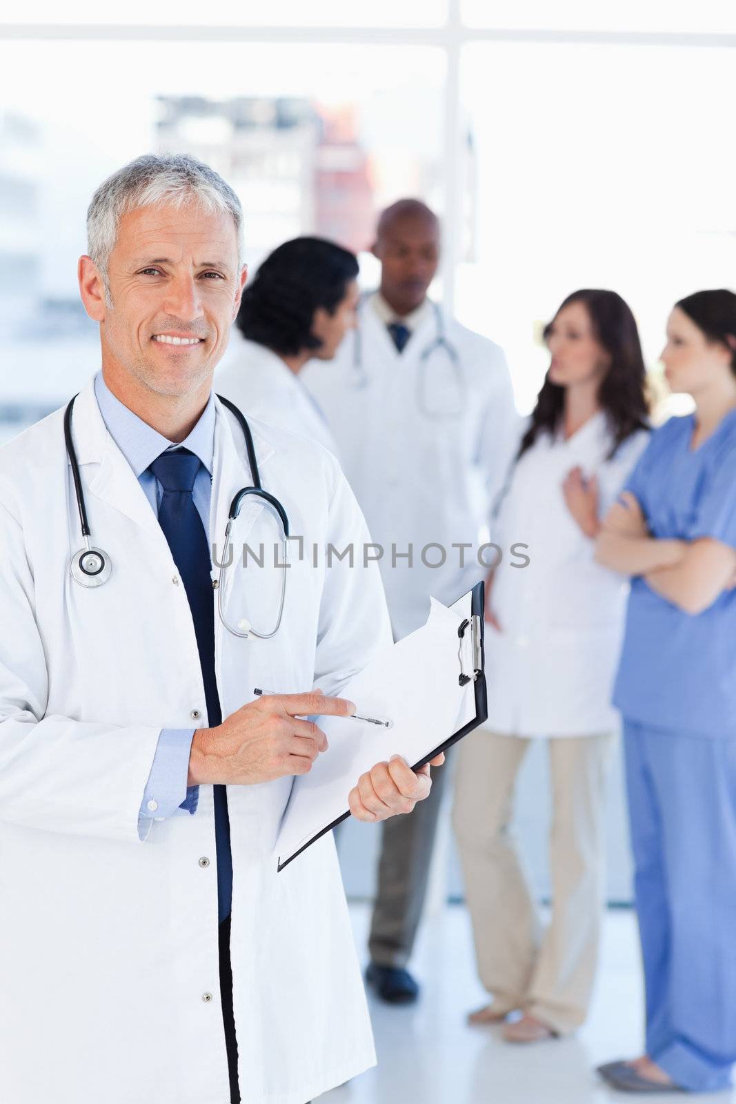 Mature doctor smiling while pointing to a sentence on his clipboard