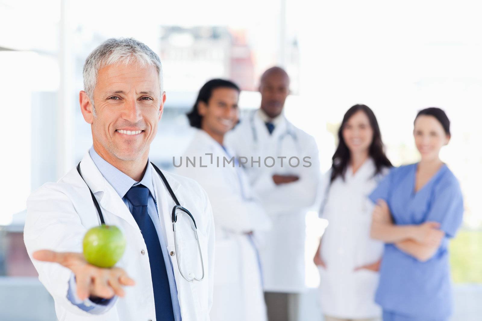 Smiling doctor holding an apple while his team is looking at him
