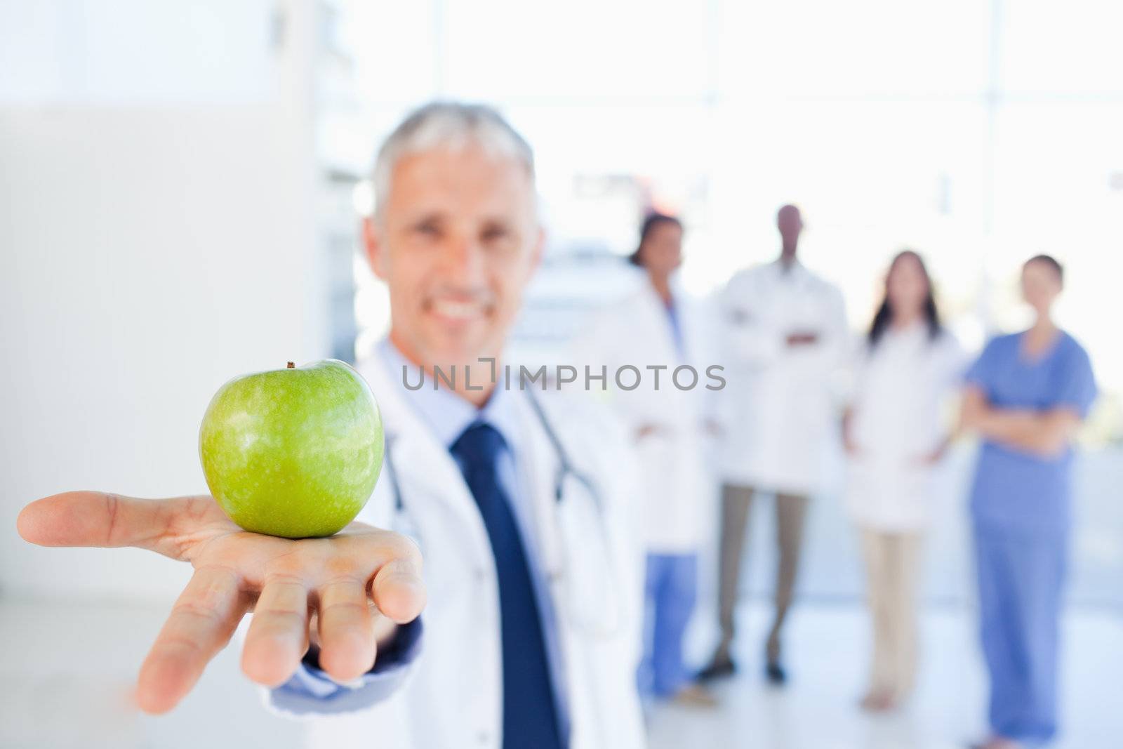 Green apple held by a doctor with a medical team behind him