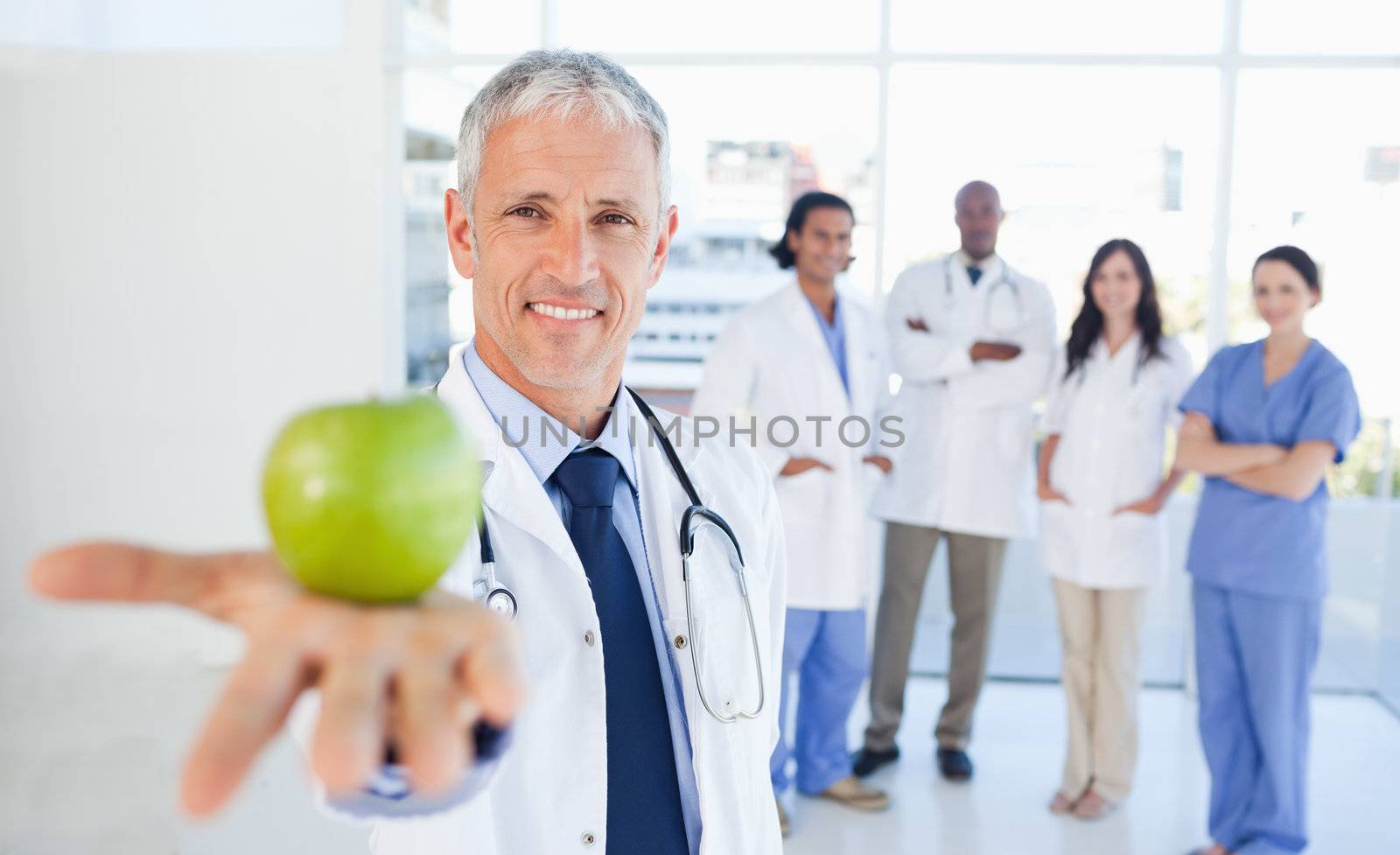 Medical interns in the background looking at their doctor who is holding an apple